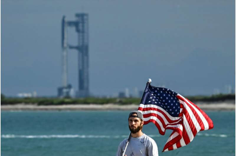 Мужчина с флагом США проходит перед гигантской ракетой Starship